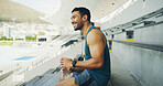 Stadium, man and smile with water bottle for fitness, hydration and running break. Outdoor, athlete person and thinking with earphones for training podcast, exercise and music for workout rest