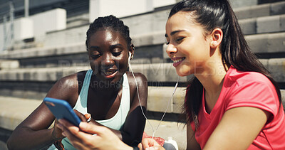 Buy stock photo Sports, earphones and girl friends outdoor with phone for listening to music, networking or social media. Laughing, fitness and female athletes on break streaming playlist on mobile app on stairs.
