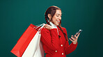 Happy woman, christmas and phone with shopping bags for online payment on a green studio background. Female person, model or shopper with smile or gifts on mobile smartphone for purchase or discount