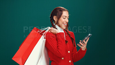 Buy stock photo Happy woman, christmas and phone with shopping bags for online payment on a green studio background. Female person, model or shopper with smile or gifts on mobile smartphone for purchase or discount