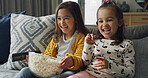 Happy girl, siblings and watching tv with popcorn on sofa for funny cartoon or movie in home. Child, sisters or kids laughing with snack or remote for online entertainment or subscription in house