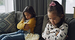 Sad girl, siblings or conflict with popcorn on sofa for fight, argument or disagreement in home. Child, kids or upset sisters with attitude or behaviour for difference or living room dispute in house