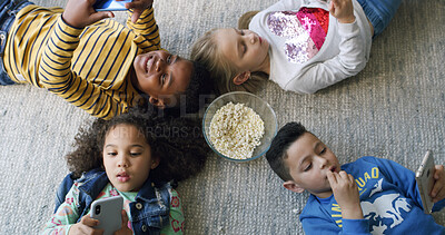Buy stock photo Popcorn, phone and group of children on floor in home for playing online games on app together. Friends, technology and top view of kids with snack and cellphone for watching movie or show in house.