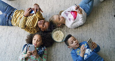 Buy stock photo Popcorn, cellphone and group of children on floor in home for playing online games on app together. Friends, technology and kids with snack and phone for watching movie, film or show from above.