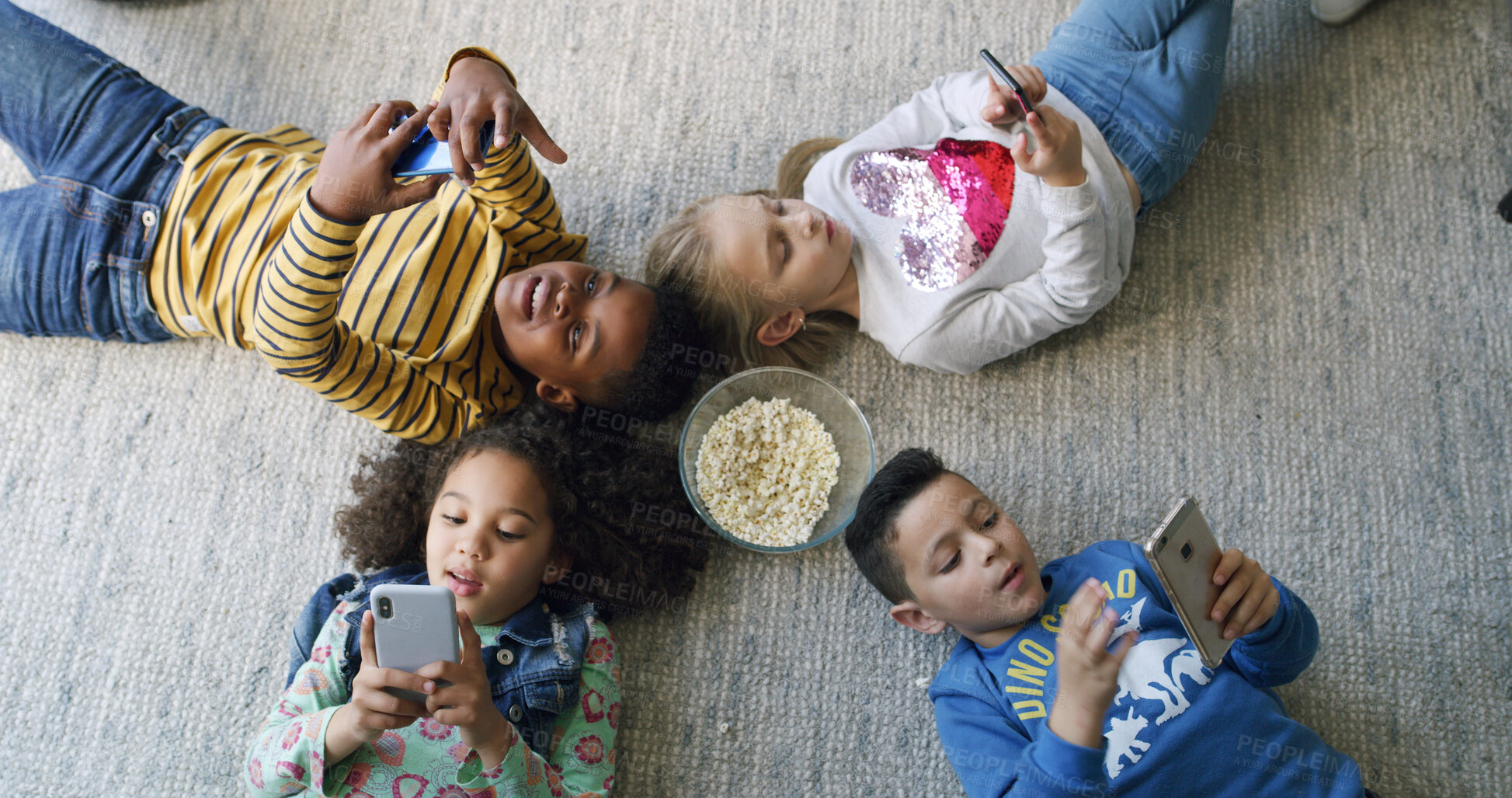 Buy stock photo Popcorn, cellphone and group of children on floor in home for playing online games on app together. Friends, technology and kids with snack and phone for watching movie, film or show from above.