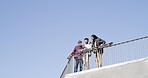 Below, friends and together with skateboard, phone and together on blue sky space. Conversation, people and gen z skater group with tech, smile and social media for fitness hobby and break for sport