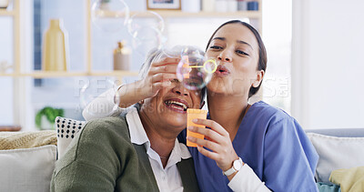 Buy stock photo Nurse, elderly woman and blowing bubbles with laugh, medical support or happy in retirement home. Soap toy, caregiver and senior patient in living room for funny game with hug, bonding and healthcare