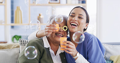 Buy stock photo Caregiver, elderly woman and blowing bubbles for laugh, medical support or happy in retirement home. Soap toy, nurse and senior patient in living room for funny game with hug, bonding and healthcare