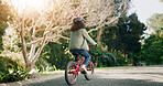 Girl, back and bicycle in neighborhood, street and ride on adventure, learning and helmet for safety. Child, bike and outdoor with cycling gear, fun and summer at park on road by trees in nature