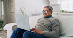 Laptop, smile and senior man on sofa reading online blog, news or email in living room at home. Happy, technology and elderly male person in retirement with computer for communication in apartment.