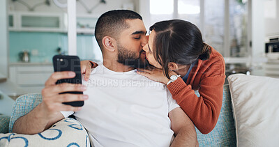 Buy stock photo Kiss, couple and selfie in home for love, care or post on social media for relationship. Photo, man and woman in living room with picture, relax and embrace partner for romantic memory together