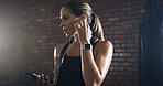 Woman, earphones and phone at gym with music, listen or mobile app with sound for training by wall. Person, audio and streaming subscription with smartphone, exercise and routine at fitness club