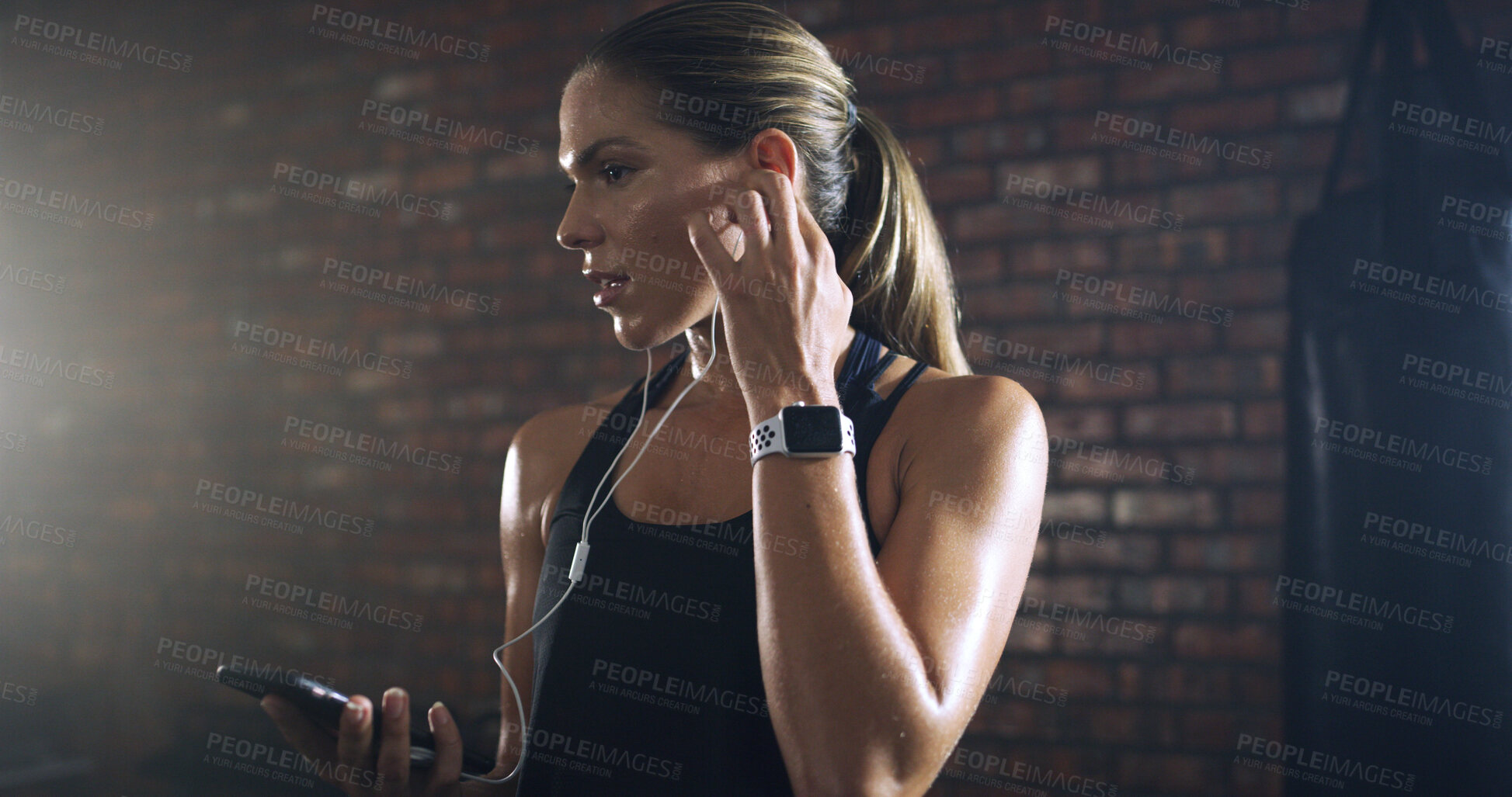 Buy stock photo Woman, earphones and phone at gym with music, listen or mobile app with sound for training by wall. Person, audio and streaming subscription with smartphone, exercise and routine at fitness club