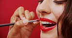 Woman, brush and lipstick for beauty in studio with makeup, facial makeover and foundation glow. Female person, artist and cosmetics with bold glamour, lip color and check results on red background