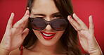 Wink, sunglasses and portrait of woman in studio for fashion, trendy style and cosmetics. Happy, aesthetic and face of confident person with accessories, makeup and red lipstick on color background