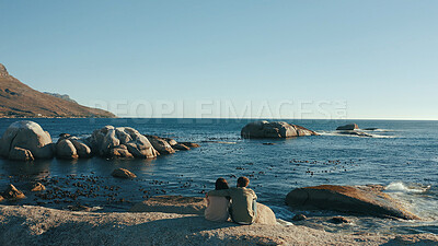 Buy stock photo Hug, rocks and back of couple by ocean for relaxing on holiday, vacation and weekend together. Dating, travel and man with woman embrace by sea, water and horizon for bonding, relationship or romance