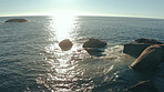 Sunrise, waves and background of ocean with rocks for holiday destination, vacation and seascape. Sunlight, sea and horizon in natural environment with coastline scenery, beach ripples and landscape
