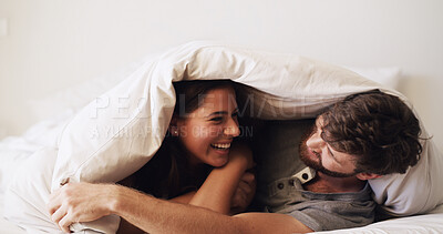 Buy stock photo Couple, laughing and cuddle in bed with happiness, moment and connection for bonding in home. Woman, man and under blanket for hug, funny memory and rest with commitment, trust and comfort in bedroom