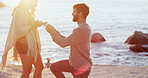 Man, woman and proposal with engagement ring at beach, kneeling and happy at sunset on vacation. Couple, question and jewelry for union, commitment and marriage offer by ocean on holiday in Spain