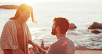 Happy woman, man and surprise with engagement ring at beach, propose and love at sunset on vacation. Couple, question and jewelry with wow, commitment or marriage offer by sea on holiday in Portugal
