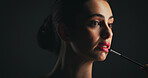 Makeup, brush and woman in studio with lipstick, beauty or facial routine with products. Cosmetics, self care and female person with tool for face cosmetology treatment for glow on black background