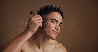 Buy stock photo Face roller, skincare and man in studio, beauty and dermatology on brown background. Mockup space, glow and person with wellness, tools and massage with cosmetics, shine and lymphatic drainage