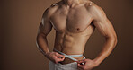 Bodybuilder, lose weight and measuring waist, hands and tape to track progress, healthy and fitness. Studio background, shirtless and checking body results, muscle and person with biceps or wellness