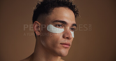 Buy stock photo Natural, eye pads and man in studio for beauty, skincare or grooming for facial routine. Happy, cosmetics and person with collagen patches for dermatology treatment by brown background with space.