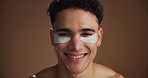 Natural, eye pads and portrait of man in studio for beauty, skincare or grooming for facial routine. Happy, cosmetics and person with collagen patches for dermatology treatment by brown background.