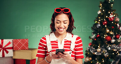 Buy stock photo Christmas, smile and woman with phone in studio for holiday, festive season or gift shopping. Xmas, mobile and happy girl with app to purchase present on internet with website on green background