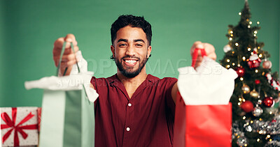 Buy stock photo Portrait, man and bags in studio for Christmas celebration, gift giving and xmas discount. Smile, male person and festive with shopping package, holiday giveaway and offer present on green background