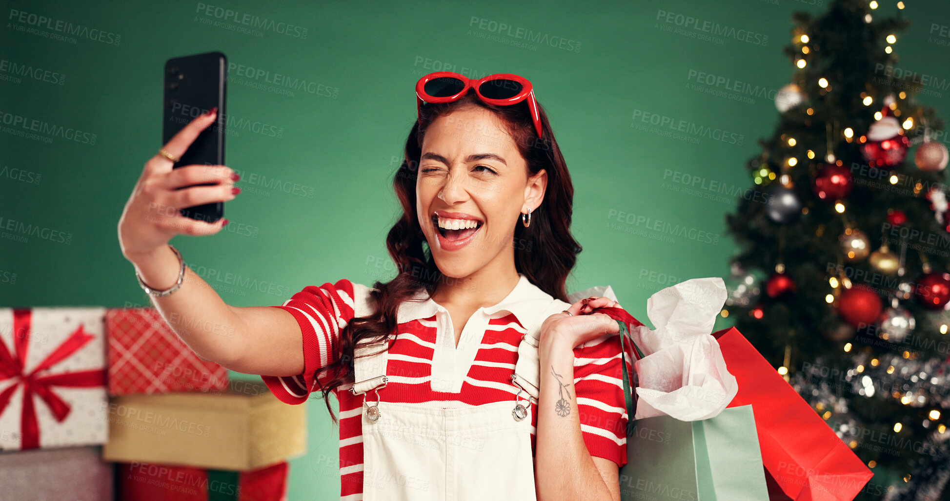 Buy stock photo Winking, woman and shopping for Christmas, selfie and memory of festive celebration and photography. Studio, person and social media post of Xmas gifts, green background or profile picture on holiday