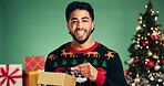 Portrait, man and present in studio for Christmas holiday, wishlist and festive celebration. Smile, male person and point with package for xmas gift, giveaway and tradition prize on green background