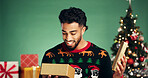Man, Christmas in studio and happy for gift, box and holiday celebration with festive season on green background. Tree, bokeh and male person with smile for present, tradition or xmas package