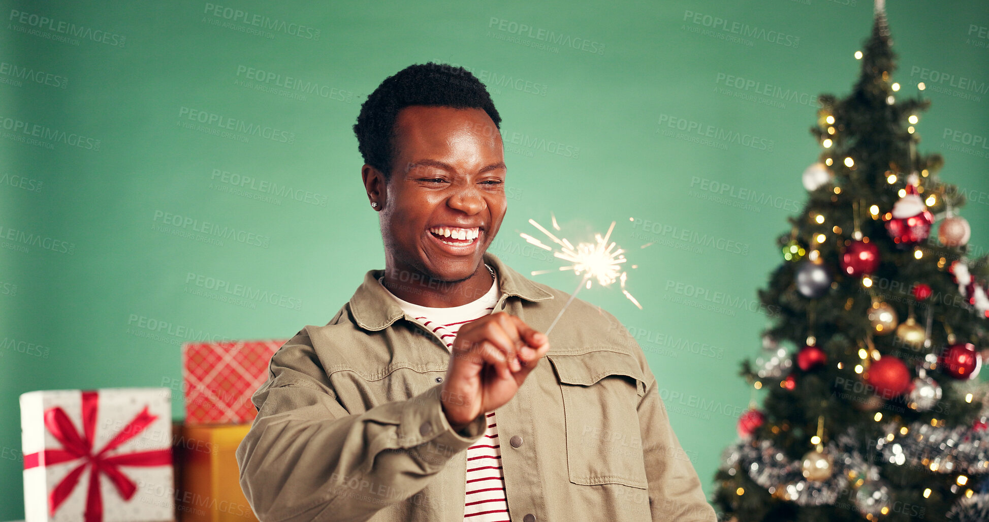 Buy stock photo Christmas, laugh and black man with sparkler in studio for festive season on green background. African person, xmas and firework for holiday celebration, funny and excited for party with present