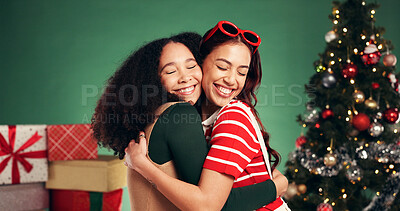 Buy stock photo Women, hug and smile in Christmas studio with friends, holiday and festive cheer for bonding. Excited, love and embrace by tree for xmas celebration, presents or decoration on green background