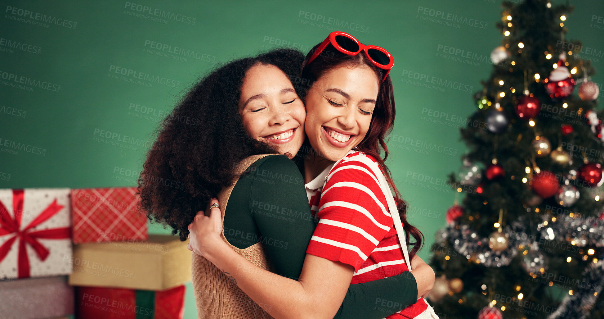 Buy stock photo Women, hug and smile in Christmas studio with friends, holiday and festive cheer for bonding. Excited, love and embrace by tree for xmas celebration, presents or decoration on green background