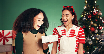 Buy stock photo Christmas, gift and surprise with friends in studio for holiday season, celebration and xmas package. Present, festive tradition and smile with women with box on green background for bonding and wow