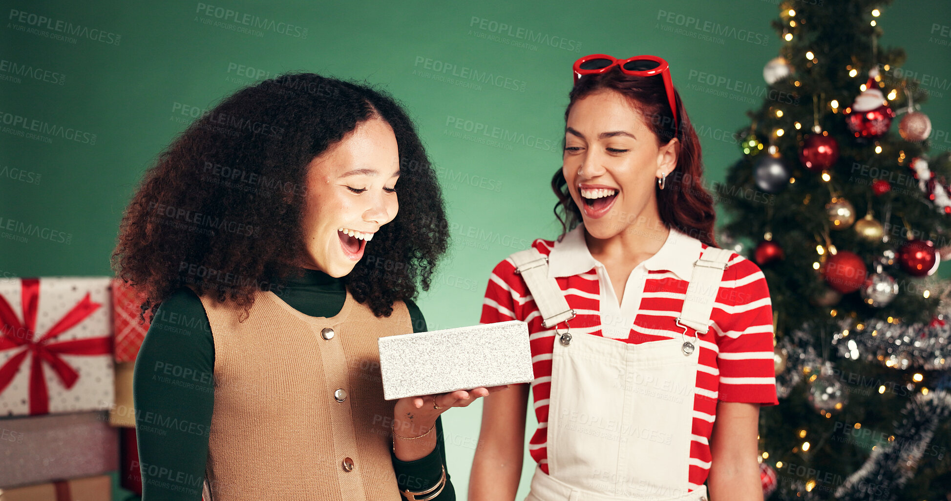 Buy stock photo Christmas, gift and surprise with friends in studio for holiday season, celebration and xmas package. Present, festive tradition and smile with women with box on green background for bonding and wow