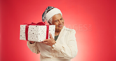 Buy stock photo Christmas, elderly woman or shake present in studio for guess, surprise or prize in retirement. Senior person, smile or gift box on red background space for festive season, Xmas tradition or secret