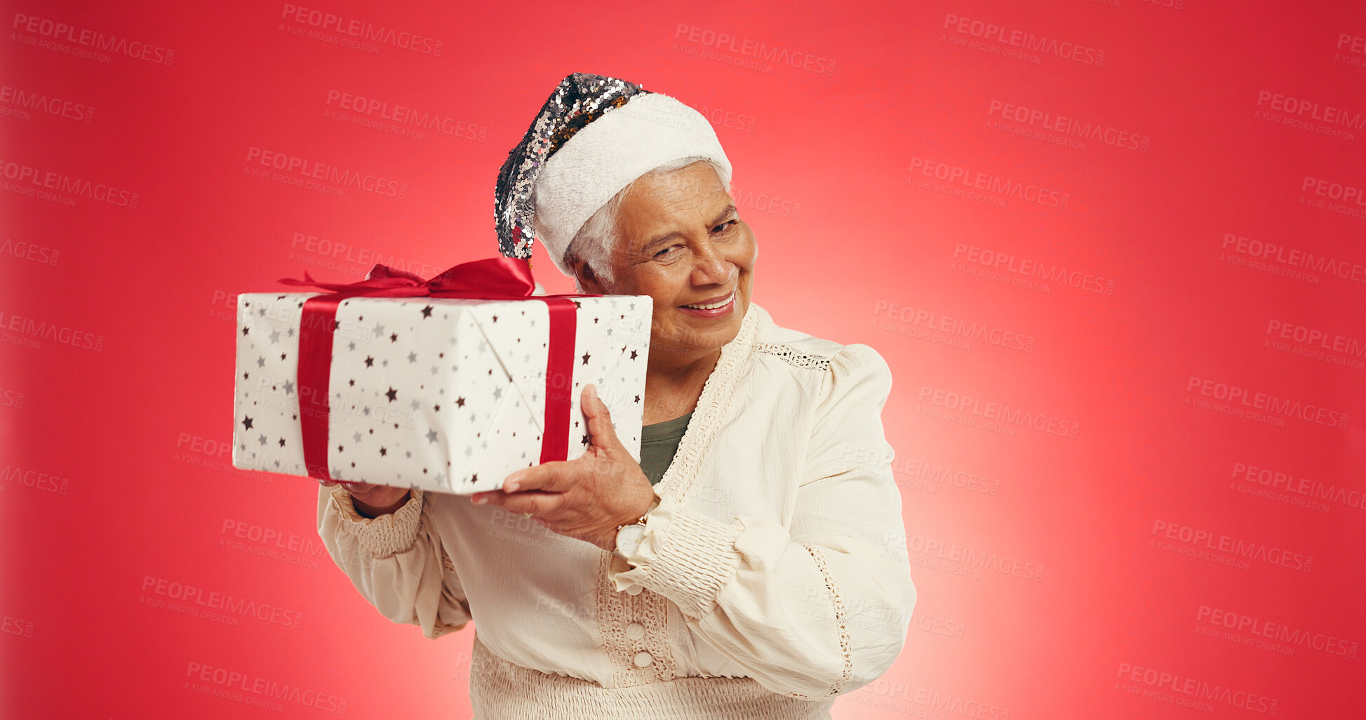 Buy stock photo Christmas, elderly woman or shake present in studio for guess, surprise or prize in retirement. Senior person, smile or gift box on red background space for festive season, Xmas tradition or secret