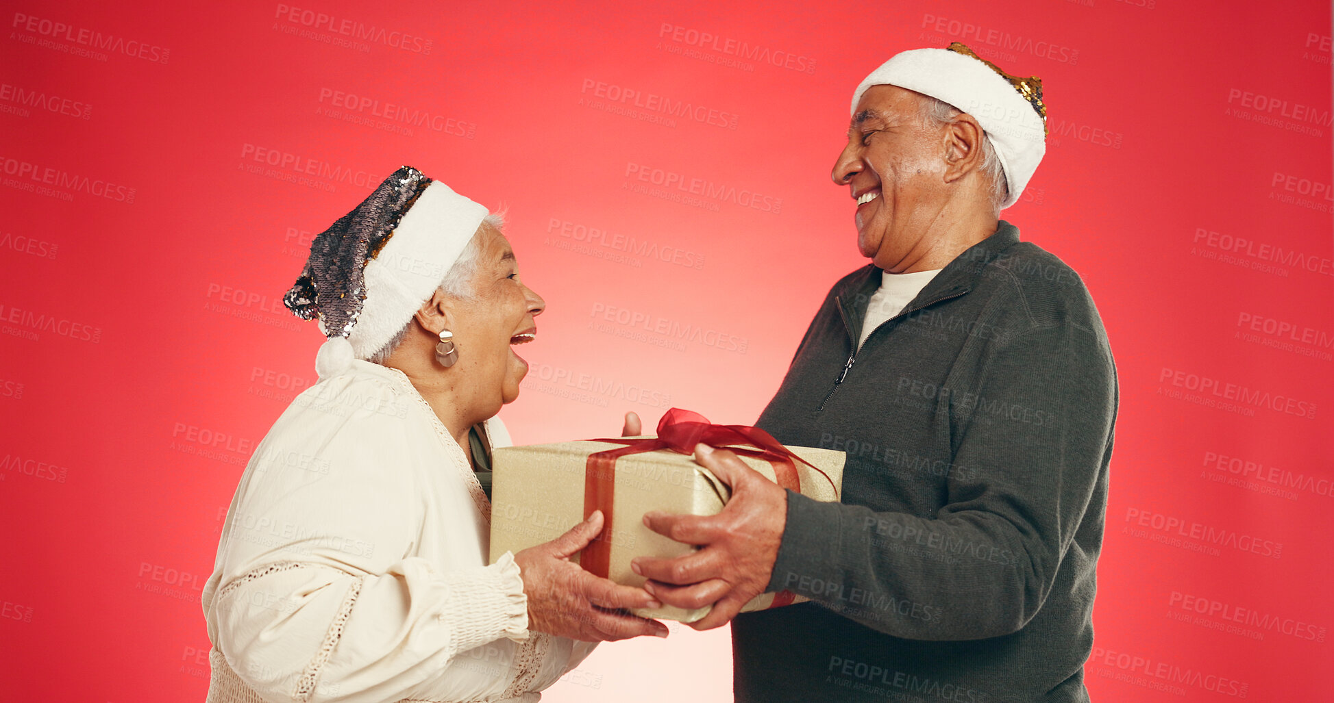 Buy stock photo Surprise, gift box and senior couple with christmas in studio with tradition, festive or holiday. Happy, santa hat and elderly man with woman for xmas present in marriage together by red background.