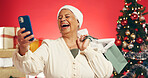 Phone, shopping bags and senior woman with christmas in studio with networking on mobile app. Laugh, gifts and elderly female person with cellphone for communication with xmas by red background.