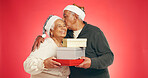 Christmas, kiss and senior couple with gift, box or giving with retirement discount in studio. Love, happy man and woman together for marriage, present or festive holiday sale on red background space