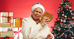 Gift box, christmas and senior woman in studio with curiosity for tradition, festive or holiday. Happy, santa hat and elderly person with present for xmas season with decorations by red background.