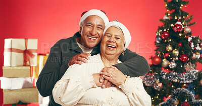 Buy stock photo Hug, Christmas and portrait of senior couple in studio with love, festive and marriage tradition. Smile, santa hat and elderly man embracing woman by xmas tree for celebration on red background.