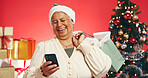 Senior, happy woman and phone with shopping bag for christmas deal on a red studio background. Elderly, female person or model with gift or mobile smartphone for december holiday or festive discount