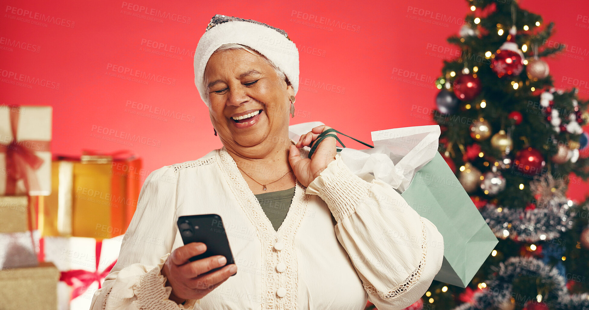 Buy stock photo Senior, happy woman and phone with shopping bag for christmas deal on a red studio background. Elderly, female person or model with gift or mobile smartphone for december holiday or festive discount