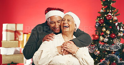 Buy stock photo Laugh, christmas and senior couple in studio with love, festive and marriage tradition. Hugging, santa hat and elderly man embracing woman by xmas tree for celebration together by red background.