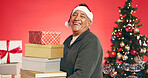 Gift boxes, christmas and senior man in studio for tradition, festive or holiday celebration. Portrait, santa hat and elderly person with presents for xmas season with decorations by red background.